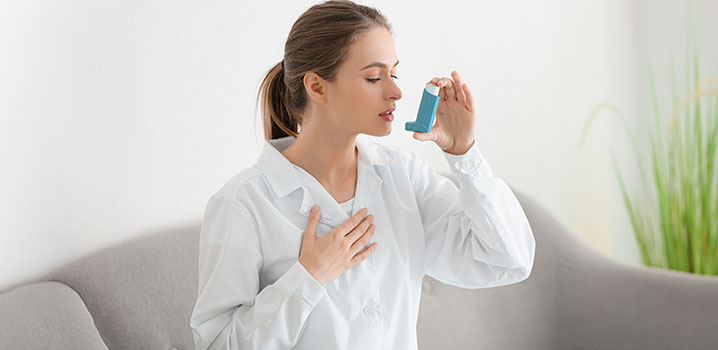 Junge Frau auf dem Sofa hält einen Inhalator in der Hand